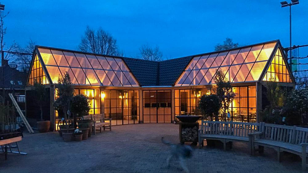 Avondfoto van glazen tuinhuis met sfeervolle verlichting